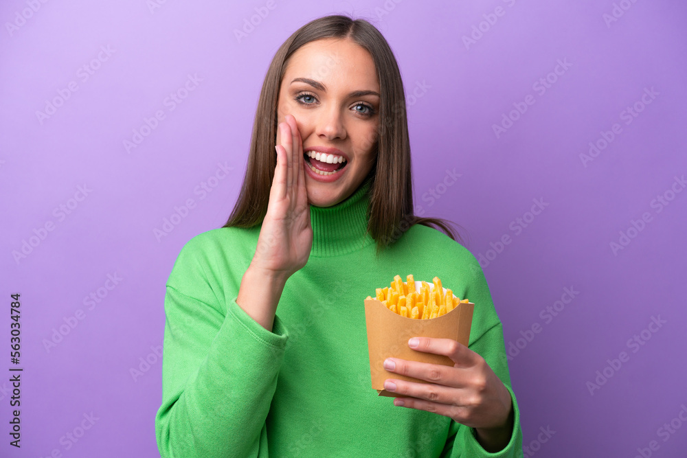 Young caucasian woman holding fried chips on purple background shouting with mouth wide open Young caucasian woman holding fried chips on purple background shouting with mouth wide open