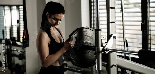 Woman adding weight on a bar as she workout in fitness gym