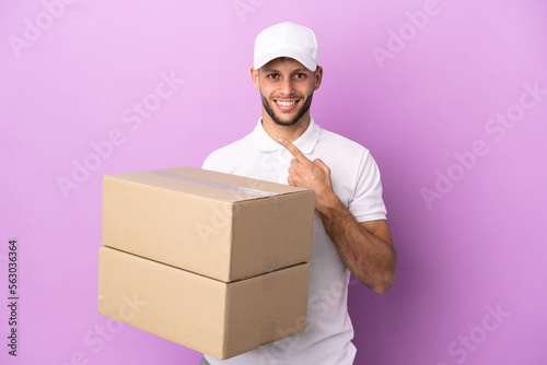 Delivery caucasian man isolated on purple background pointing to the side to present a product © luismolinero