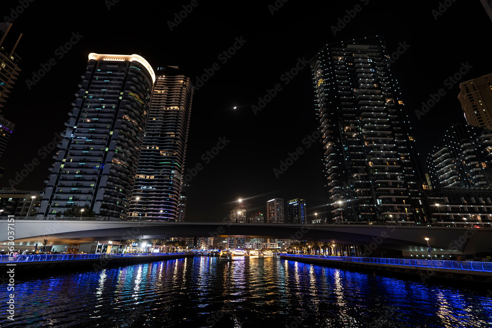 Naklejka premium beautiful night view of dubai marina skyscrapers from the water side on the river. Bridge in Dubai Marina illuminated at night