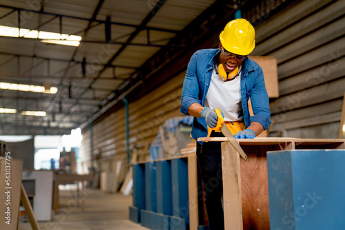 Front view of African American carpenter man use sawing wood to work with timber on table during work in factory workplace area. photo