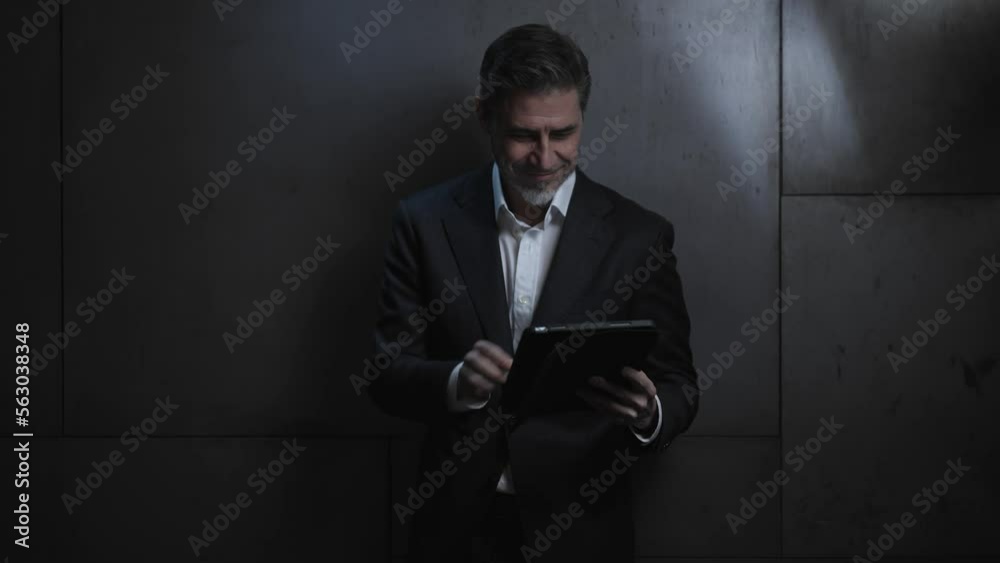 Portrait of happy mature businessman with tablet computer. Entrepreneur standing in front of dark wall. Confident older, middle aged, mid adult, man in his 40s or 50s in business casual. Portrait of happy mature businessman with tablet computer. Entrepreneur standing in front of dark wall. Confident older, middle aged, mid adult, man in his 40s or 50s in business casual.