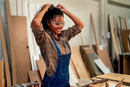 African American carpenter woman stand with setting up her hair and smile during work in wood factory workplace.