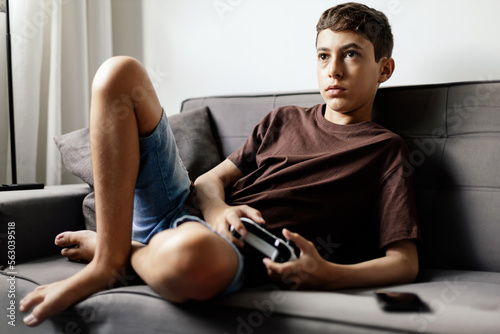 Teenager playing video games at home. Teenager sitting on sofa playing video game with bad posture. Teenager health concept.