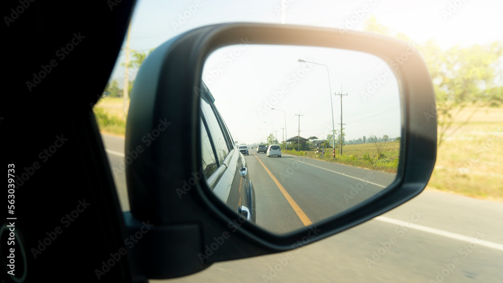 Beside of gray car in the mirror wing of car. driving on the asphalt road with yellow and other cars drive behind.