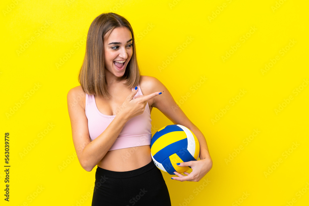 Young woman playing volleyball isolated on yellow background pointing finger to the side and presenting a product