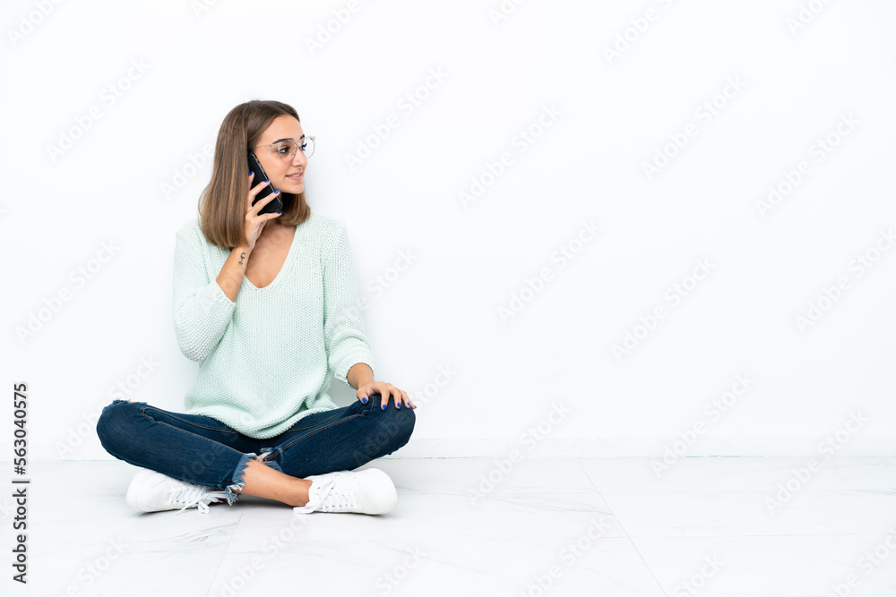 Young caucasian woman sitting on the floor isolated on white background keeping a conversation with the mobile phone with someone Young caucasian woman sitting on the floor isolated on white background keeping a conversation with the mobile phone with someone