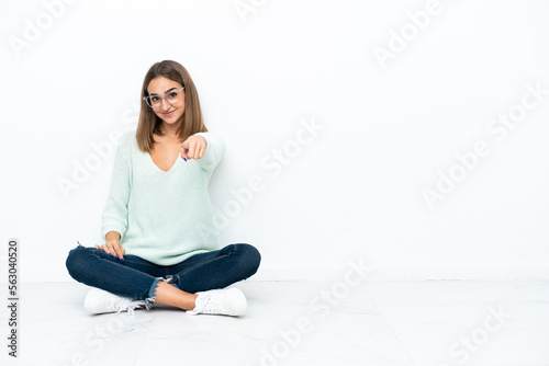 Young caucasian woman sitting on the floor isolated on white background points finger at you with a confident expression