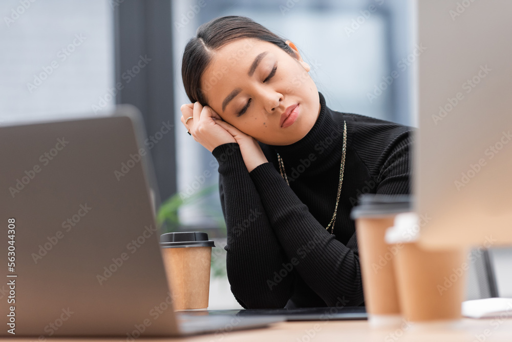 Sleepy asian designer sitting near computers and coffee in office. Sleepy asian designer sitting near computers and coffee in office.