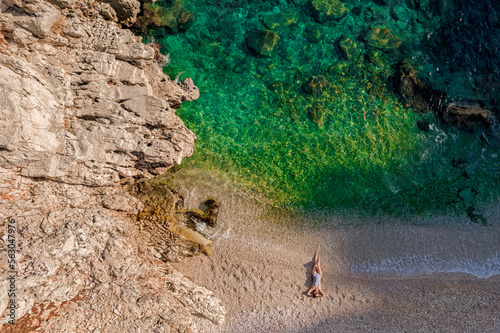 Young girl in a swimsuit lies on an empty beach next to a clear sea. Drone shot top view.