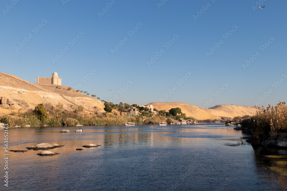 Beautiful landmark of Nile river bank shore with traditional construction village in the desert dunes and mountains with faluca boat sailing