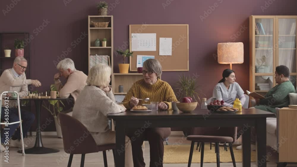Diverse group of seniors spending their leisure time at day room of comfortable nursing home, chatting, playing chess and resting
