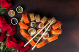 Heart shaped Valentine day sushi set. Classic sushi rolls, philadelphia, maki set for two, with two pairs of chopsticks for Valentine's dating dinner, with rose flowers bouquet on dark background