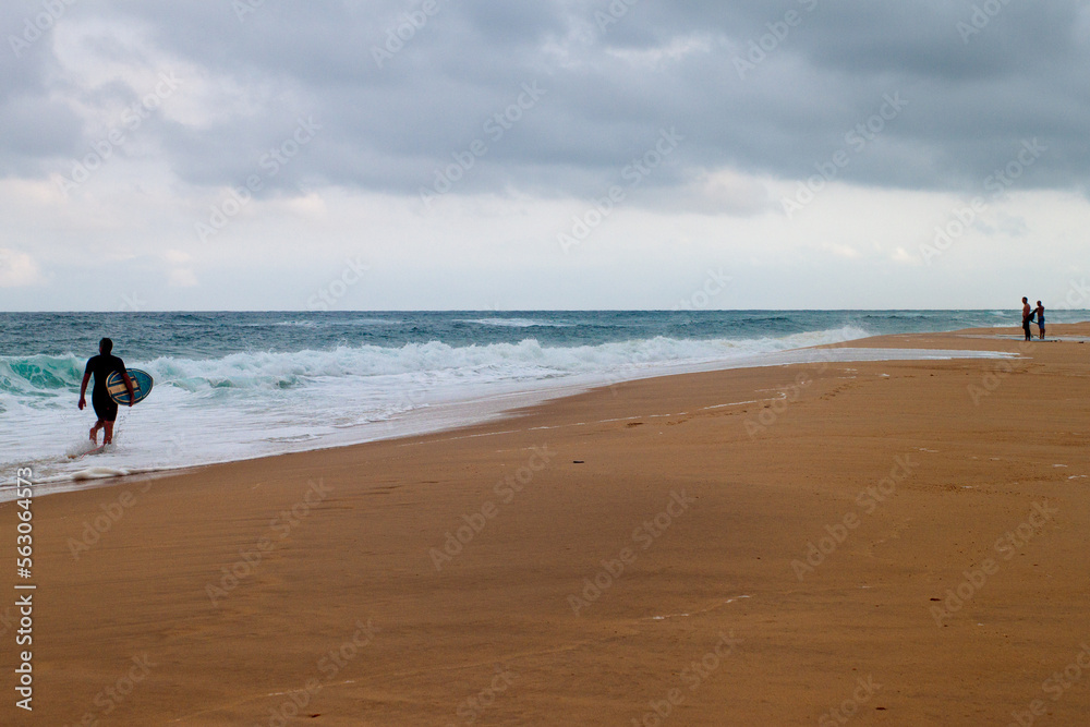 The waves of the Atlantic Ocean in the Landes in France in bad weather. Unidentifiable surfers observe the ocean and the waves.
