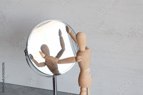 A mannequin wooden man stands on a light background and looks in the mirror.