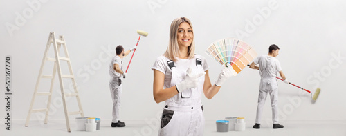 Female house painter holding a color swatch palette and pointing and other workers painting photo