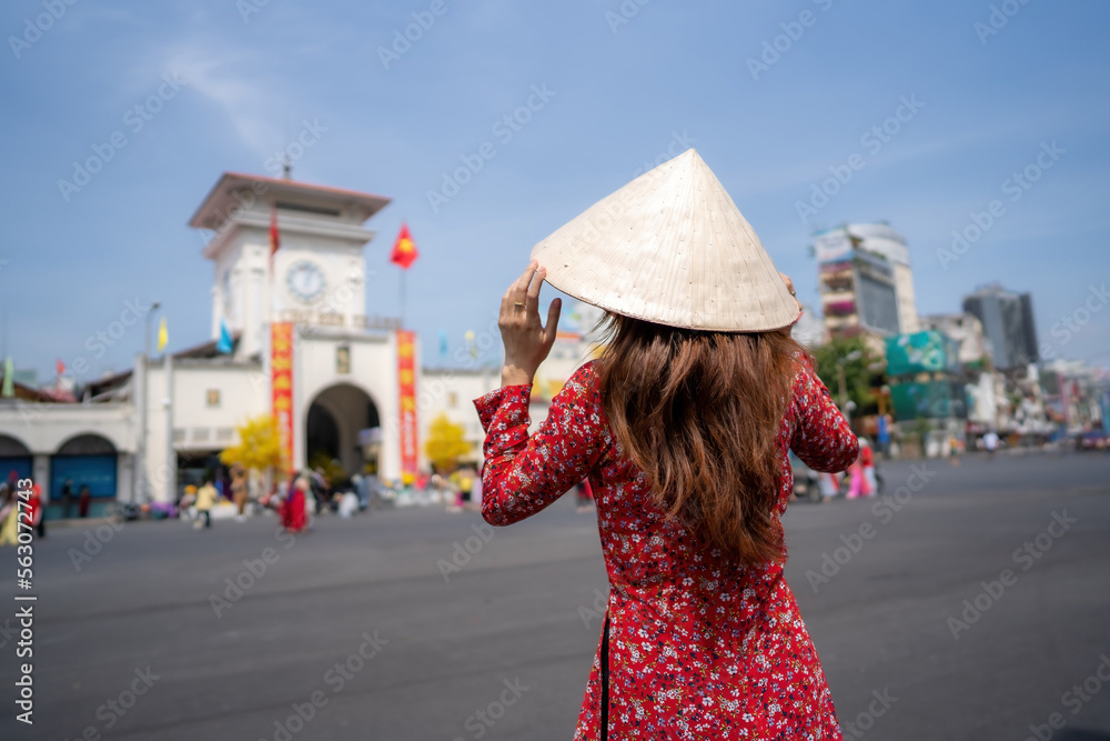 Vietnamese girl with Ao Dai dress walking in front of Ben Thanh market , Ho Chi Minh city, Vietnam. Ao dai is famous traditional costume for woman in Vietnam. Tet holiday and New Year.