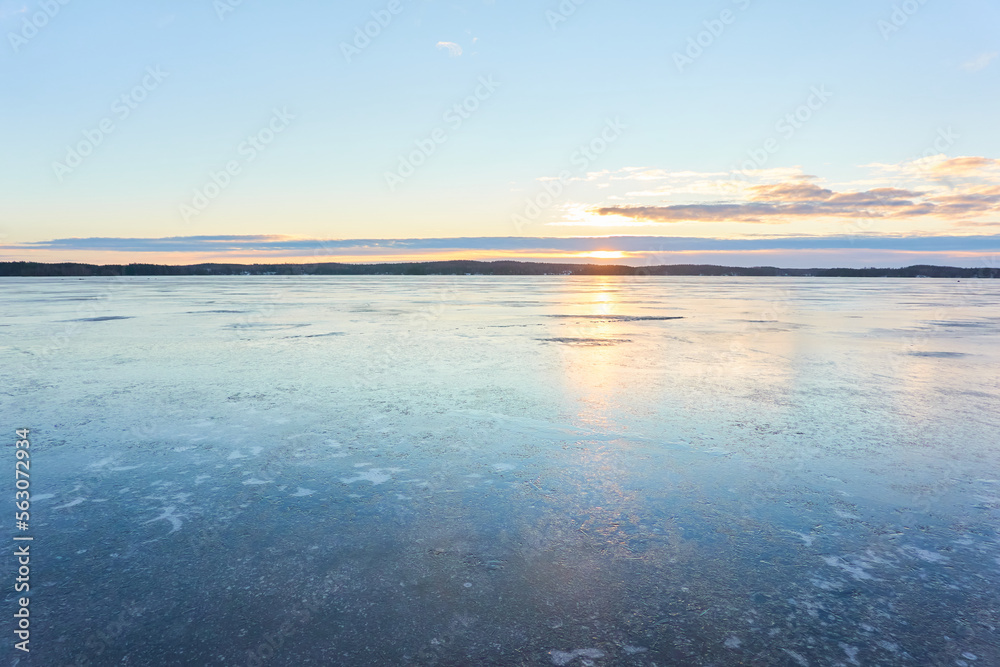 Panoramic view of the forest lake at sunrise. Evergreen trees. Soft sunlight. Frozen water surface. Finland. Winter landscape. Nature, ecology, ecotourism, cold weather, climate change themes