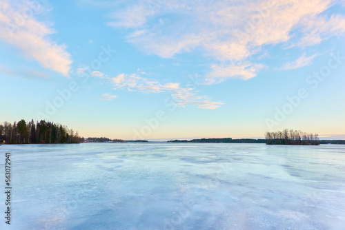 Panoramic view of the forest lake at sunrise. Evergreen trees. Soft sunlight. Frozen water surface. Finland. Winter landscape. Nature  ecology  ecotourism  cold weather  climate change themes