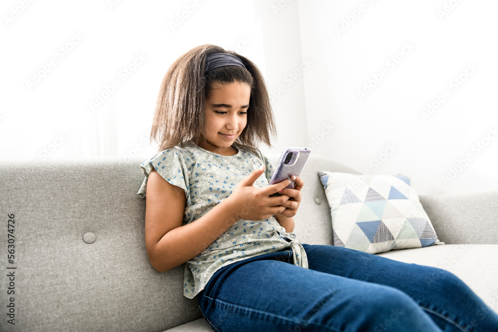 Obraz premium American teen girl using phone sit on sofa at home,