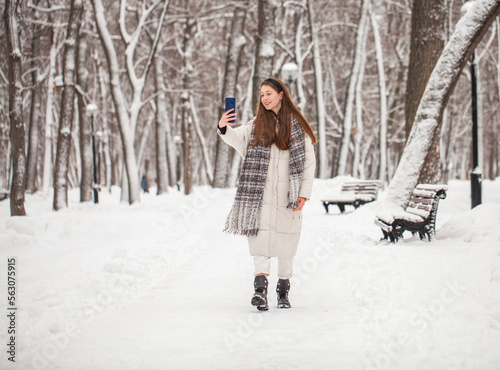 Young beautiful woman in a gray down jacket in a winter snowy park © Andrey_Arkusha