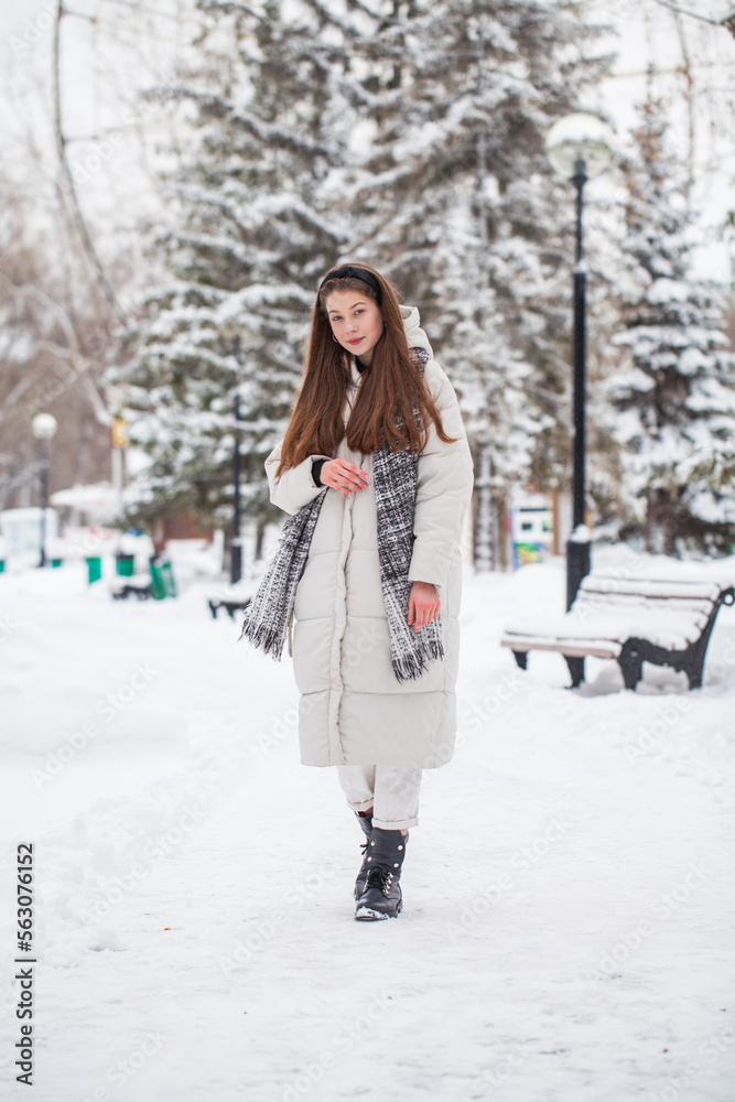 Young beautiful woman in a gray down jacket in a winter snowy park Young beautiful woman in a gray down jacket in a winter snowy park