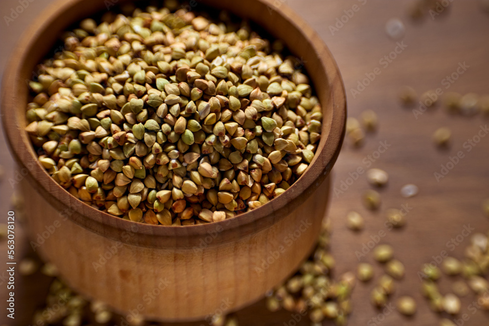 Unprocessed green buckwheat in a wooden bowl on a wooden board. Unprocessed green buckwheat in a wooden bowl on a wooden board.