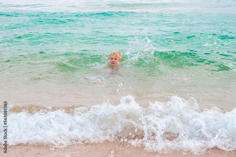 A blond boy learns to swim in the seawater on a summer day at the coast. Fun vacation. A blond boy learns to swim in the seawater on a summer day at the coast. Fun vacation.