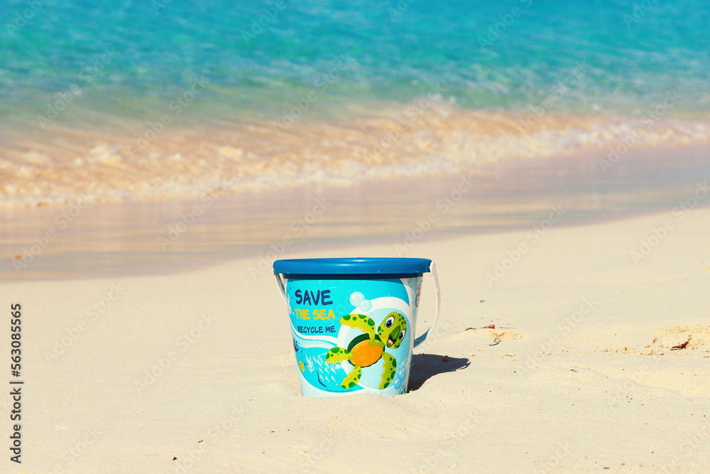 Save the sea, recycle me. Kids or baby blue bucket on the beach. Environmental care Save the sea, recycle me. Kids or baby blue bucket on the beach. Environmental care
