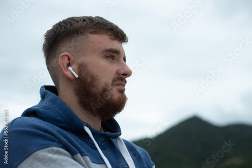 Portrait of bearded handsome pensive thoughtful guy, listen music in earphones, young upset sad frustrated man on natural mountain background, thinking with a serious face © Евгений Шемякин