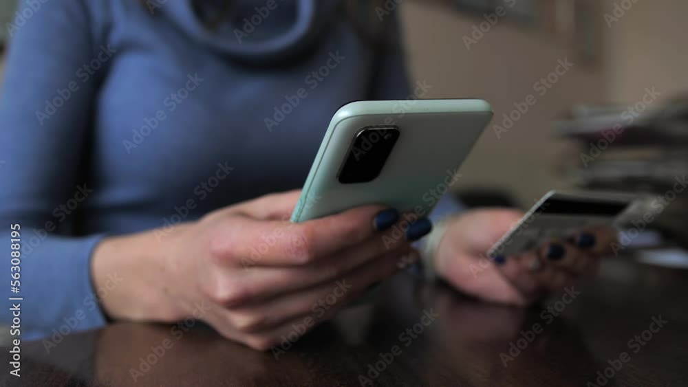 The girl makes an online payment using a smartphone by entering a credit card number on the marketplace site. Close-up of a mobile phone and a credit card in female hands. Woman doing online shopping. The girl makes an online payment using a smartphone by entering a credit card number on the marketplace site. Close-up of a mobile phone and a credit card in female hands. Woman doing online shopping.
