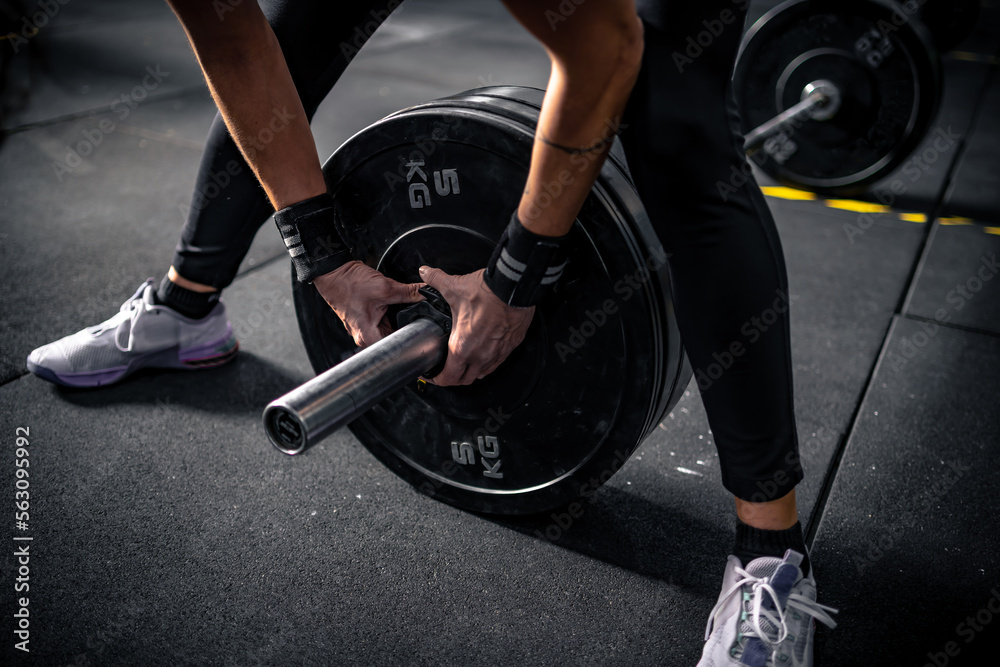 Girl in a gym preparing to lift a barbell by adjusting the lateral clasps. Girl in a gym preparing to lift a barbell by adjusting the lateral clasps.