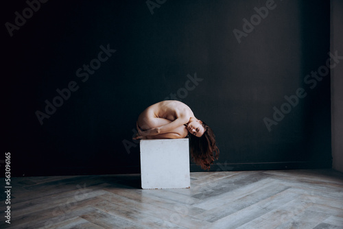 Beautiful, natural naked girl artistic posing at a stylish and fashionable nude photo shoot as a model in a photo studio with a transparent cape and bandage and looks like art