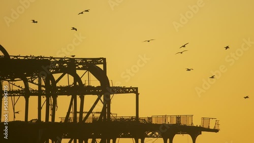 Top of Brighton ruined west pier, pan left across dilapidated frame, birds perched evening light silhouette