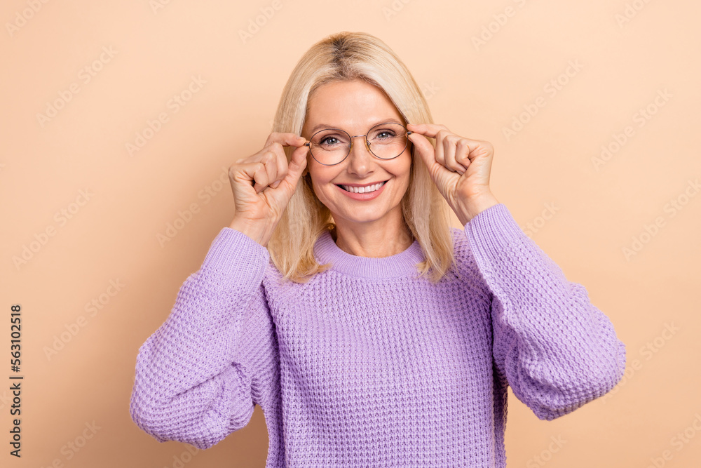 Photo of satisfied pleasant nice retired lady blond hairdo wear knit sweater hands touching glasses isolated on beige color background