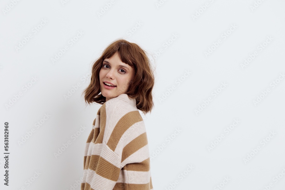 a sweet, pleasant woman with a short haircut stands on a light background in a stylish beige, striped sweater and standing sideways smiles affably at the camera a sweet, pleasant woman with a short haircut stands on a light background in a stylish beige, striped sweater and standing sideways smiles affably at the camera
