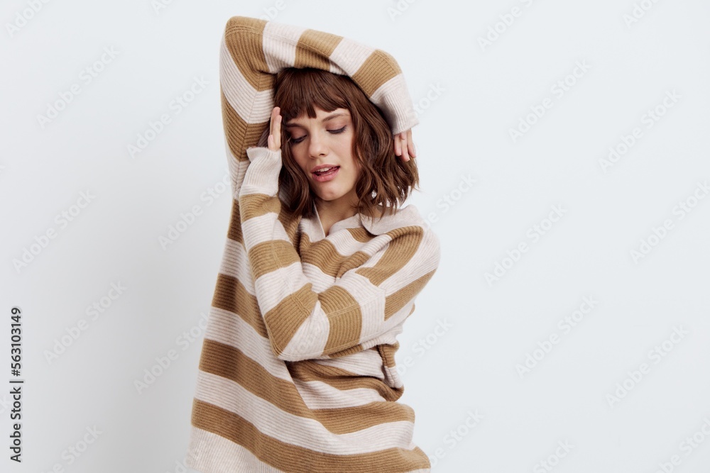 photo on a light background of beautiful, attractive woman standing in a stylish striped sweater, relaxed posing with her hands near her face with her eyes closed. A photo with an empty space photo on a light background of beautiful, attractive woman standing in a stylish striped sweater, relaxed posing with her hands near her face with her eyes closed. A photo with an empty space