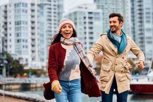 Cheerful couple having fun while holding hands along city quay. photo