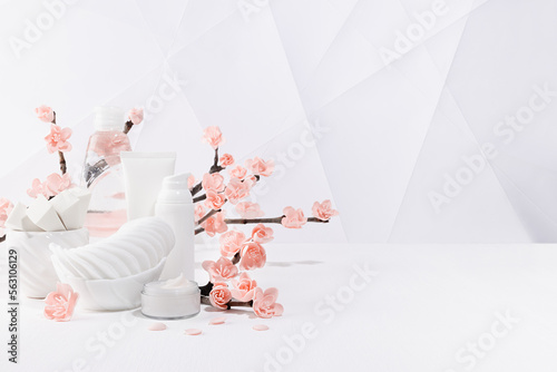 Cosmetic products for makeup, cleansing skin in white bottles, branch of spring pink sakura flowers, petals, toiletry, elegant light bathroom interior in geometric futuristic asian style, copy space.