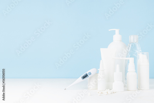 Health and pharmacy remedies for prevent and teraphy disease and illness - difference white bottles mockup, sprays, salve, pills and 36,6 thermometer on white table and blue wall, copy space. photo