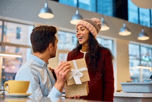 Cheerful woman surprising her boyfriend with present for their anniversary. photo