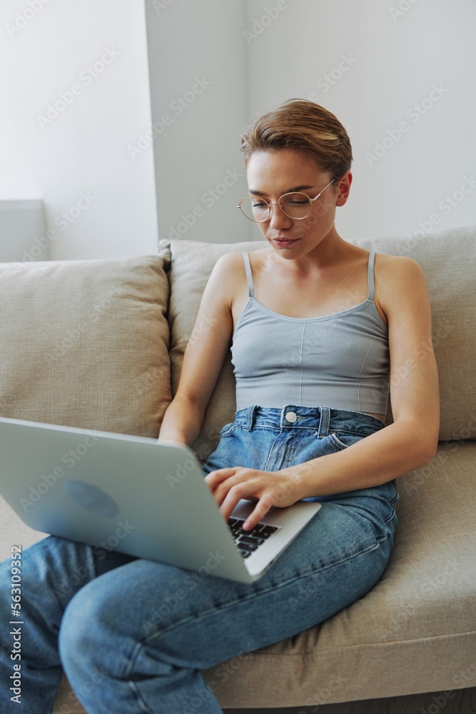 Teenage girl freelancer with laptop sitting on couch at home smiling in home clothes and glasses with short haircut, lifestyle with no filters, free copy space Teenage girl freelancer with laptop sitting on couch at home smiling in home clothes and glasses with short haircut, lifestyle with no filters, free copy space