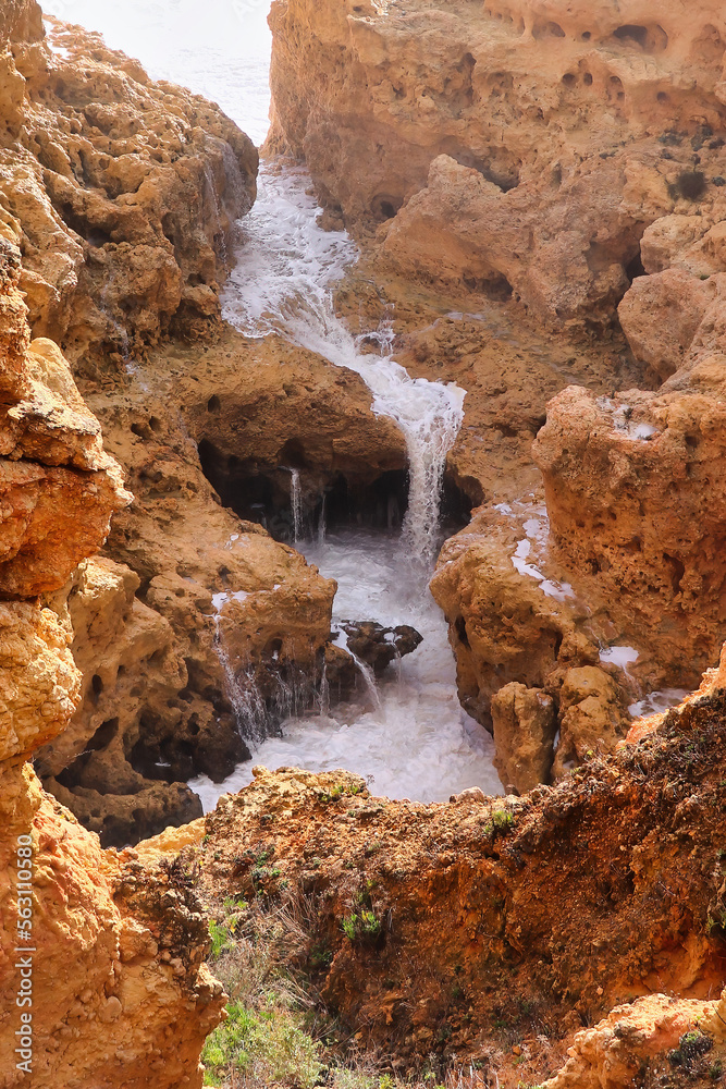 Water running over rocks into a small pool at the Atlantic Ocean in Algarve, Portugal on a warm winter day.