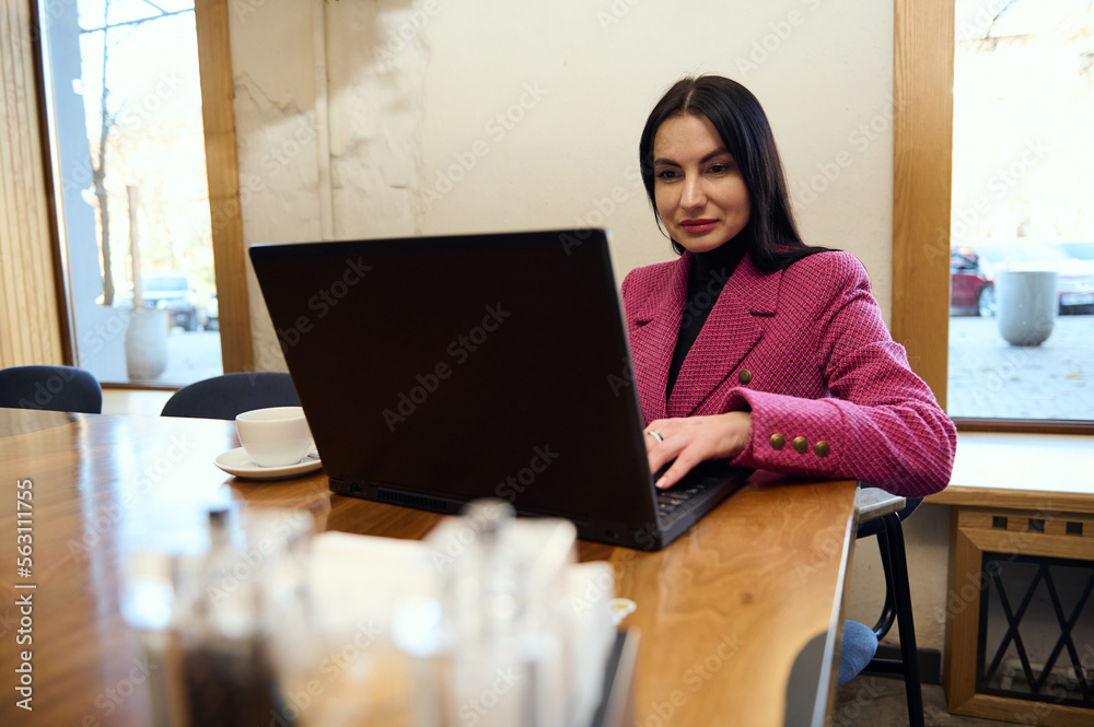 Confident Caucasian woman entrepreneur in purple casual jacket, working remotely on laptop in a coffee shop interior. Successful business lady telecommuting, planning new actions for her business plan Confident Caucasian woman entrepreneur in purple casual jacket, working remotely on laptop in a coffee shop interior. Successful business lady telecommuting, planning new actions for her business plan