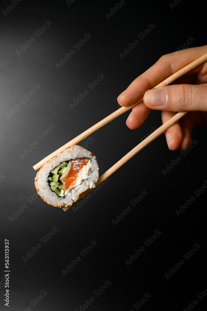 hand holding one piece of roll california with smoked salmon garnished sesame seeds with bamboo chopsticks hand holding one piece of roll california with smoked salmon garnished sesame seeds with bamboo chopsticks