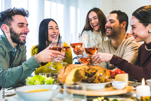 Group of happy friends toasting rose wine glasses   Young smiling friends having fun at dinner party home-Cheerful guys enjoying time together at table eating meals-Dining Concept-Focus on glasses 