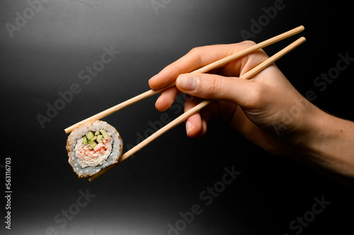 Female hand gently holding one piece of roll california with snow crab meat garnished sesame seeds with bamboo chopsticks