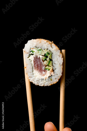 Close-up of roll california with salmon garnished sesame seeds in bamboo chopsticks