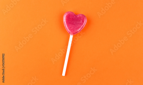 Pink lollipop in shape of a heart on orange background