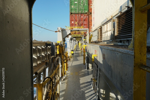 View on main deck from port side and open ventilation covers in a row of 
side of hatch covers installed on container vessel. In background are containers and blue sky.